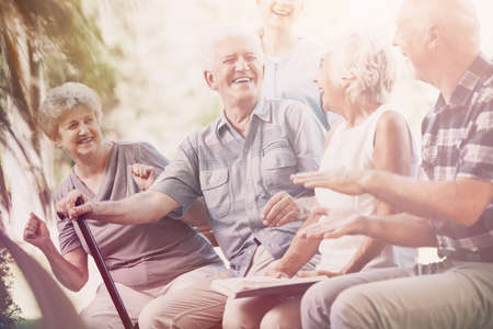 Smiling senior man with walking stick relaxing with elderly woman and friendsの写真素材