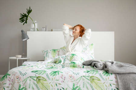 Smiling beautiful redhead woman waking up in comfortable bed with patterned sheets