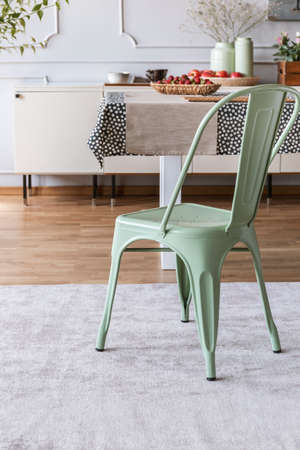 Mint green chair on grey carpet at table in rustic dining room interior with lamp and wall with molding. Real photoの写真素材
