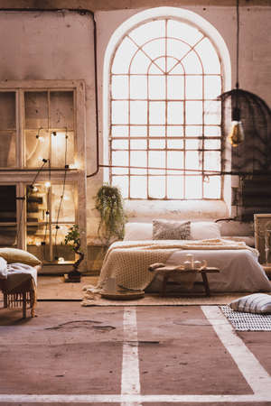 Window above bed with pillows in spacious bright loft interior with plant and lights. Real photoの写真素材