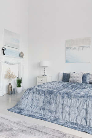 Plants and lamp next to blue bed in white minimal bedroom interior with posters. Real photoの写真素材