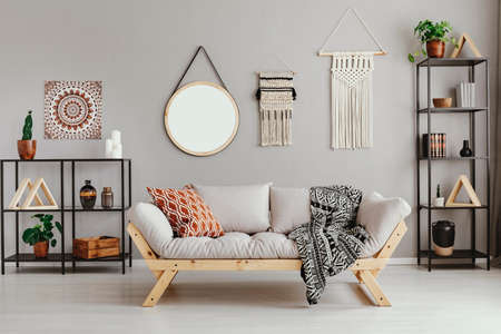 Macrame, mirror and ethno graphic on beige wall in stylish living room interior with metal furniture...