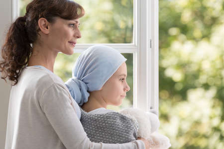 Smiling mother supporting sick daughter wearing headscarf during treatmentの写真素材