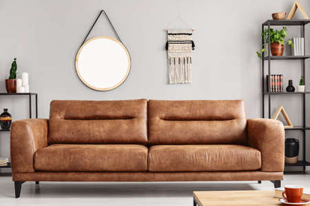 Mockup of round mirror on grey wall in living room interior with brown leather settee. Real photoの写真素材
