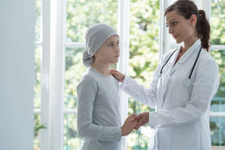 Nurse helping sick kid with cancer wearing headscarf in the hospital