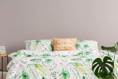 Gold cushion placed on king-size bed with leafy bedding in real photo of room interior with grey wallの写真素材
