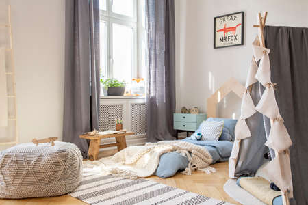 Pouf and tent in scandinavian bedroom interior with drapes at window and poster above bed. Real photoの写真素材