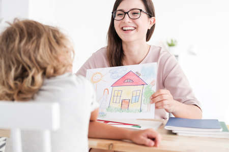 Smiling psychologist with home picture and child in a family support centre