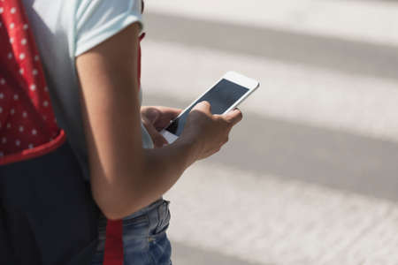 Close-up on a kid with a smartphone while walking through pedestrian crossing