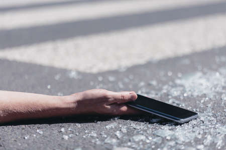 Close-up on a person with smartphone in a hand after accident on a pedestrian crossingの写真素材