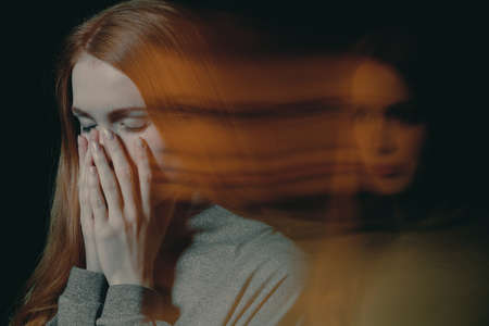 Blurred picture of young beautiful redhead girl with obsessive compulsive disorder covering her mouth and closing her eyesの写真素材