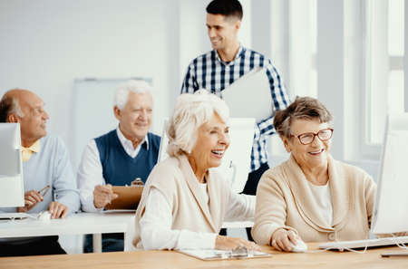 Group of active elderly people learning from young teacher how to use computer at third age university classesの写真素材