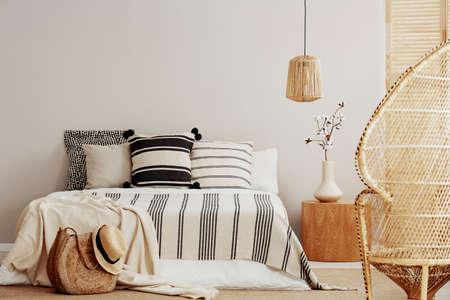 Copy space on white empty wall of bright trendy bedroom with flower in vase on wooden nightstand,...