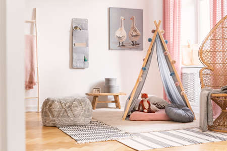Patterned pouf on carpet next to tent with cushions in white kid's room interior with poster. Real photoの写真素材