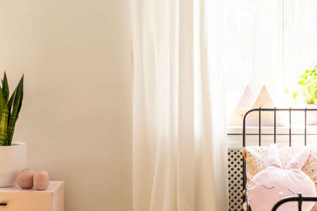 Drapes at window in white child's bedroom interior with rabbit pillow on bed and plant. Real photoの写真素材