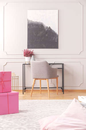 Painting on a wall, chair next to a desk and pink birthday boxes in a daily room interior