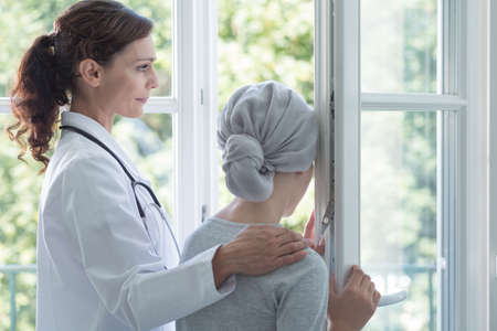 Caring doctor in white uniform supporting sick girl with cancer during chemotherapyの写真素材