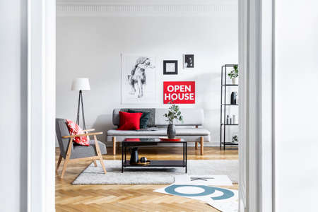 Table on carpet next to armchair and settee in living room interior with posters and lamp. Real...