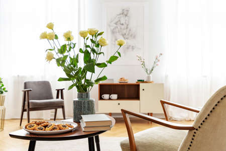 Armchair at table with flowers, books and food in bright apartment interior with windows. Real photoの写真素材