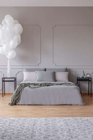 Copy space on the empty grey wall of fashionable bedroom with king size bed and black wooden nightstandsの写真素材