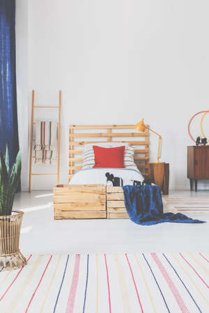 Real photo of an oldschool bedroom interior with wooden boxes, bed and striped rugの写真素材