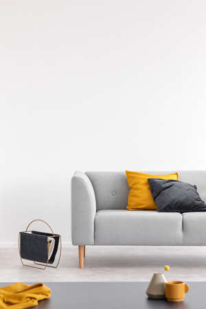 Yellow and black cushion on grey sofa in white loft interior with table and copy space. Real photoの写真素材