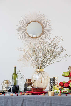 Glass vase with flowers in the middle of dining room table set with food and fruitsの写真素材