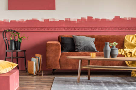 Plants in black vases on wooden chair next to magazine rack in living room with ombre wall and brown velvet cornerの写真素材