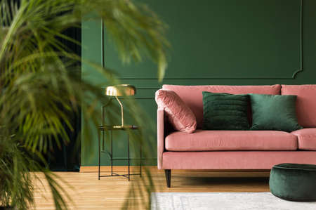Emerald green pillows on pastel pink couch in stylish living room interior with dark green wallの写真素材