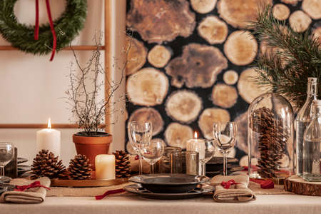 Dining room table set for christmas, wine glasses, cones and black plates on linen tableclothの写真素材