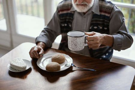 Lonely senior man sitting at kitchen table drinking teaの写真素材