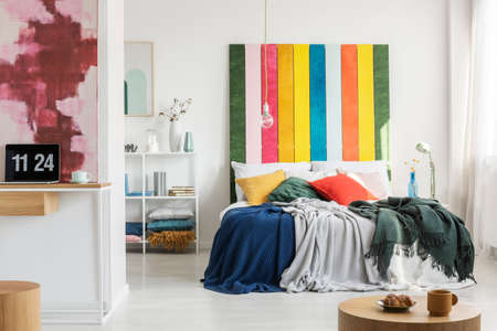Modern, open space apartment interior with a home office in the foreground and a bedroom with a colorful bedhead in the background. Real photoの写真素材