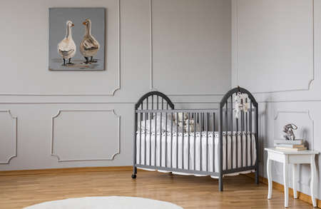 Poster on grey molding wall in baby's bedroom interior with bed next to white table. Real photo