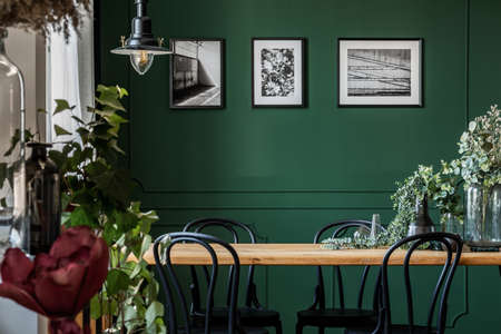 Green flowers in glass vase on long wooden table with black chairs in elegant living room