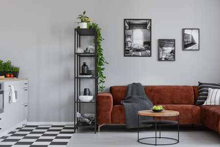 Round coffee table with green apples in the bowl in front of brown velvet sofa in small studio...