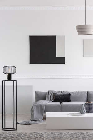 Fashionable industrial black lamp next to scandinavian sofa in bright living roomの写真素材