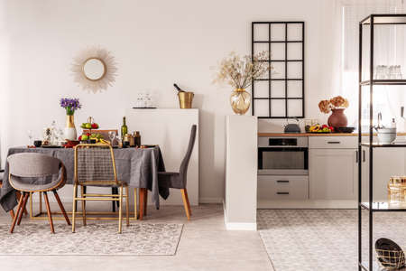 Stylish open plan kitchen and dining room interior with white cupboard and long table with grey...