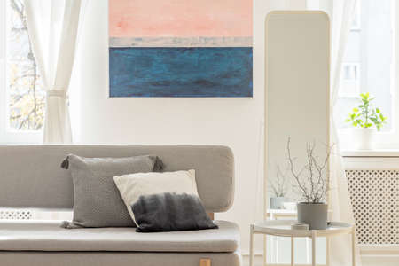 Plant in grey pot on white coffee table next to stylish grey couch with pillowsの写真素材