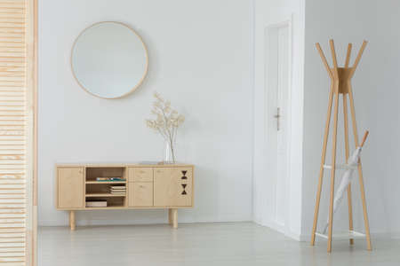 Wooden hanger with white umbrella in real photo of entrance hall interior with cupboard with books...