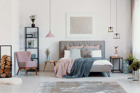 Paste pink armchair and lamp in elegant bedroom interior with comfortable bed with pillows, blanket and duvet, warm carpet on floorの写真素材
