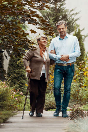 Smiling man walking with happy elderly woman in the garden