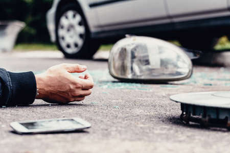 Human's hand on the ground next to broke car mirror and mobile phone after a crashの写真素材