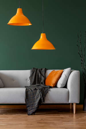 Orange lamps on a green wall and sofa in a simple living room interior