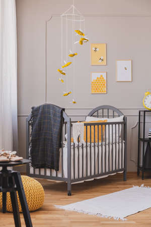 Installation with yellow and black bees above grey wooden crib with blanket and pillowの写真素材