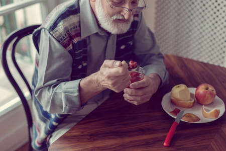 Senior grandfather with grey hair and beard sitting alone in the kitchen eating breakfastの写真素材
