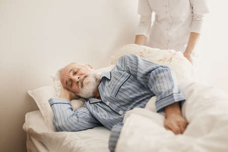 Sick elderly man wearing blue pajama lying in bed at nursing homeの写真素材