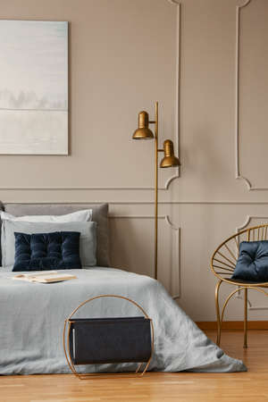 Stylish golden lamp next to king size bed with blue bedding and dark blue pillows