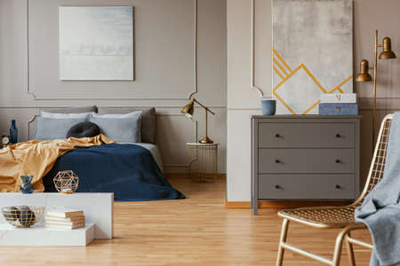Modern lamp on nightstand table next to king size bed in grey bedroom interior