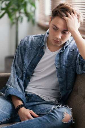 Sad teenage student sitting alone at home waiting for his father