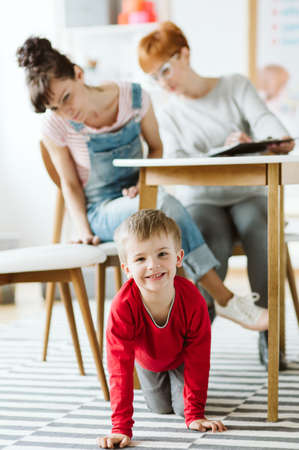 Rude kid sitting under the table during therapy for ADHD with his mother and professional therapistの写真素材
